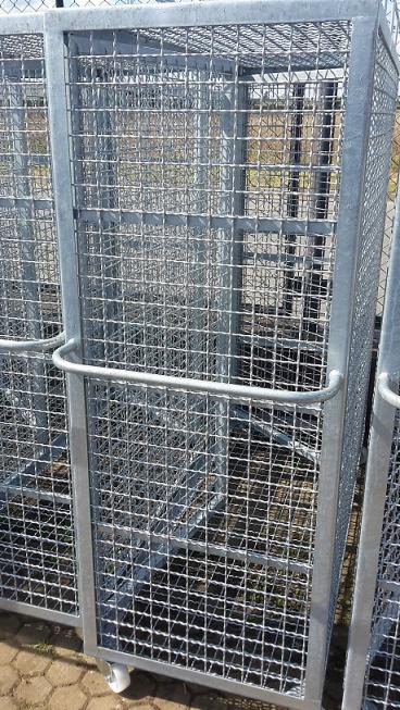 Metalowe, ocynkowane wózki-klatki z siatki na kółkach, ustawione obok siebie na zewnątrz, z widocznym tłem zieleni i elementów infrastruktury.