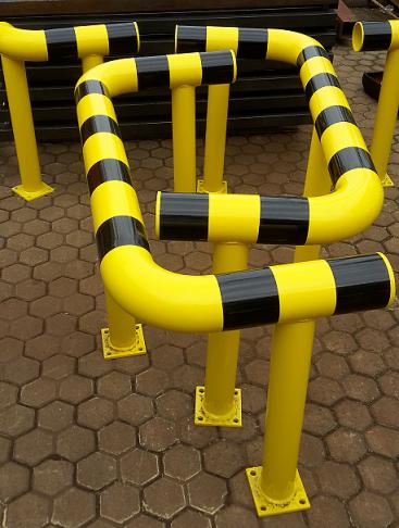 Żółto-czarne, metalowe słupki ochronne z rur na sześciokątnej kostce brukowej, tworzące barierę.