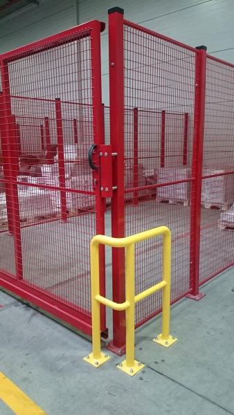 Czerwona siatka ochronna z żółtą barierką w hali magazynowej w Dzierżoniowie, widoczne palety z towarem w tle.