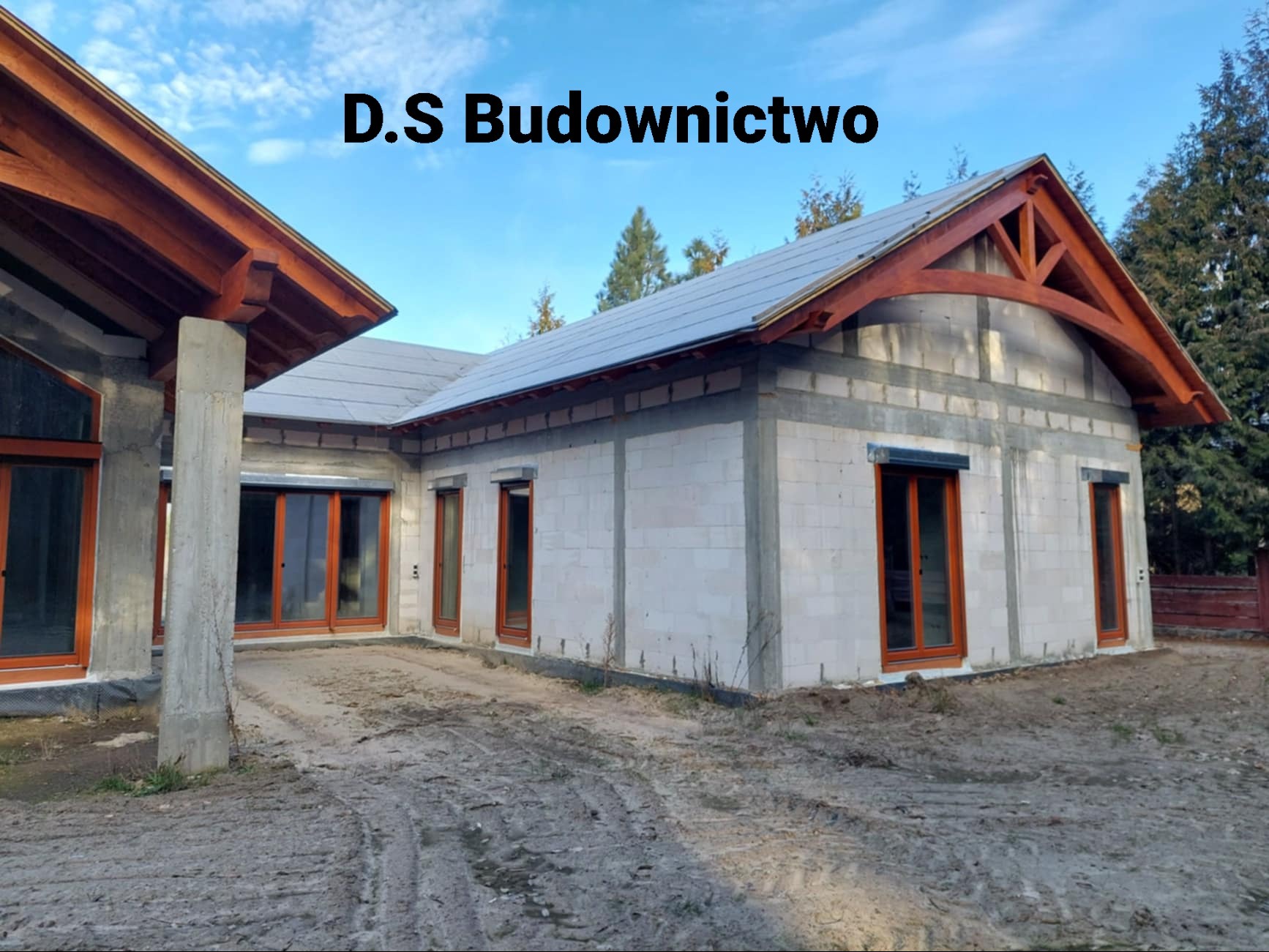 Dom murowany w trakcie budowy, widoczne ściany z betonu komórkowego, drewniana konstrukcja dachu i okna z roletami zewnętrznymi.