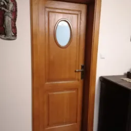 Klasyczne drzwi wewnętrzne z drewna w odcieniach brązu, z owalnym przeszkleniem i ozdobną płaskorzeźbą na ścianie obok.