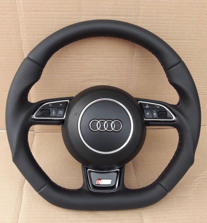 Czarna, skórzana kierownica Audi z perforowanymi bokami i czerwonymi szwami, widoczne logo Audi oraz przyciski sterowania.