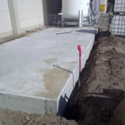 Wylany betonowy fundament pod budynek przemysłowy, widoczny wykop i wbita łopata z czerwoną rączką.