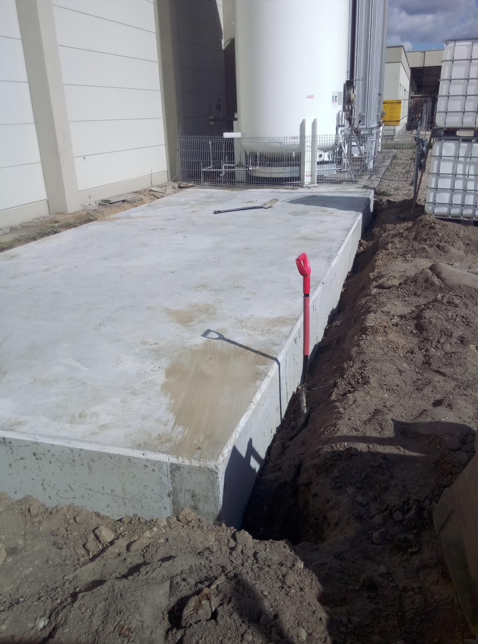 Wylany betonowy fundament pod budynek przemysłowy, widoczny wykop i wbita łopata z czerwoną rączką.