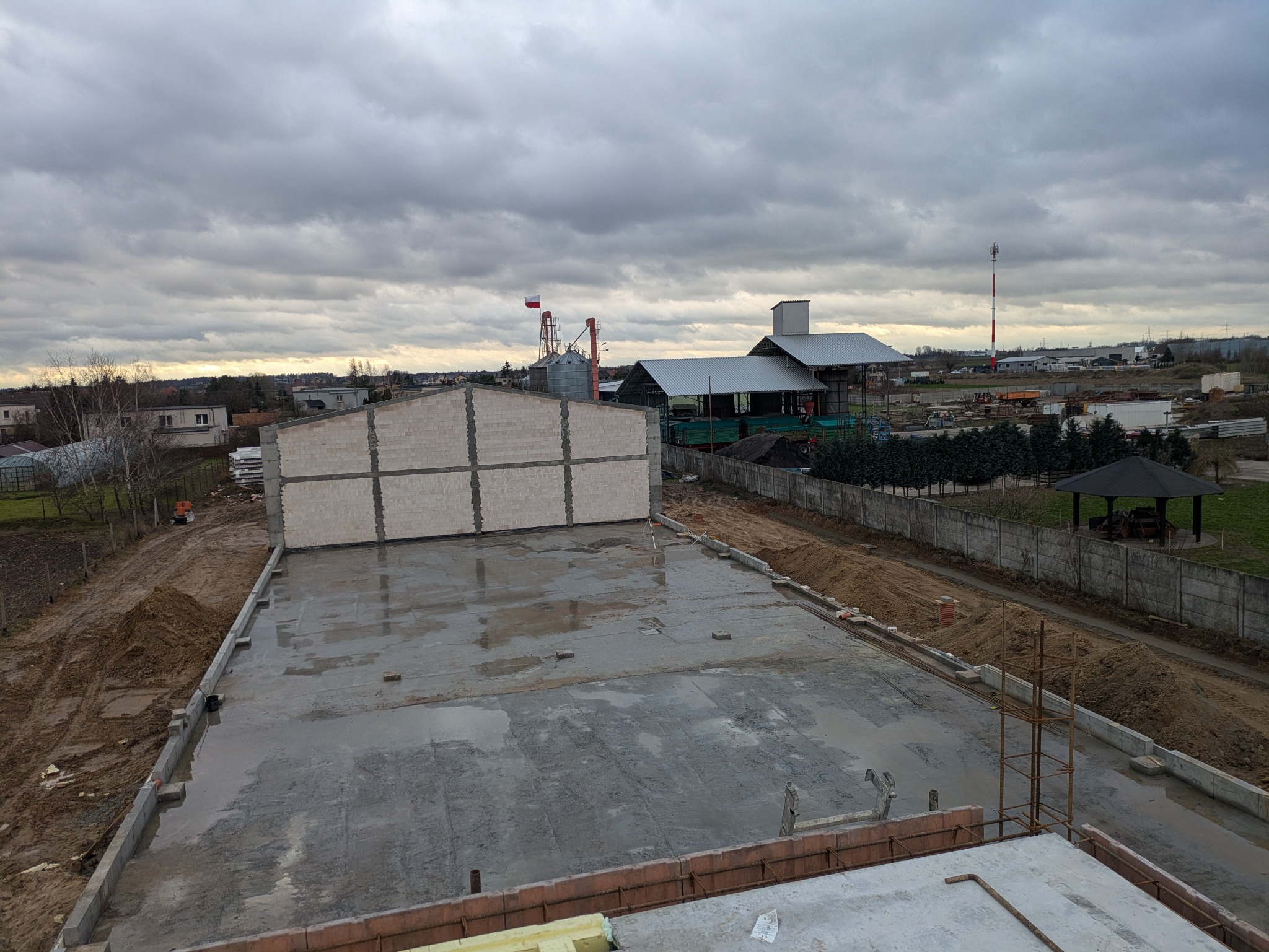 Wylany fundament pod budynek z częściowo wzniesionymi ścianami z betonu komórkowego, widok z góry na plac budowy w pochmurny dzień.