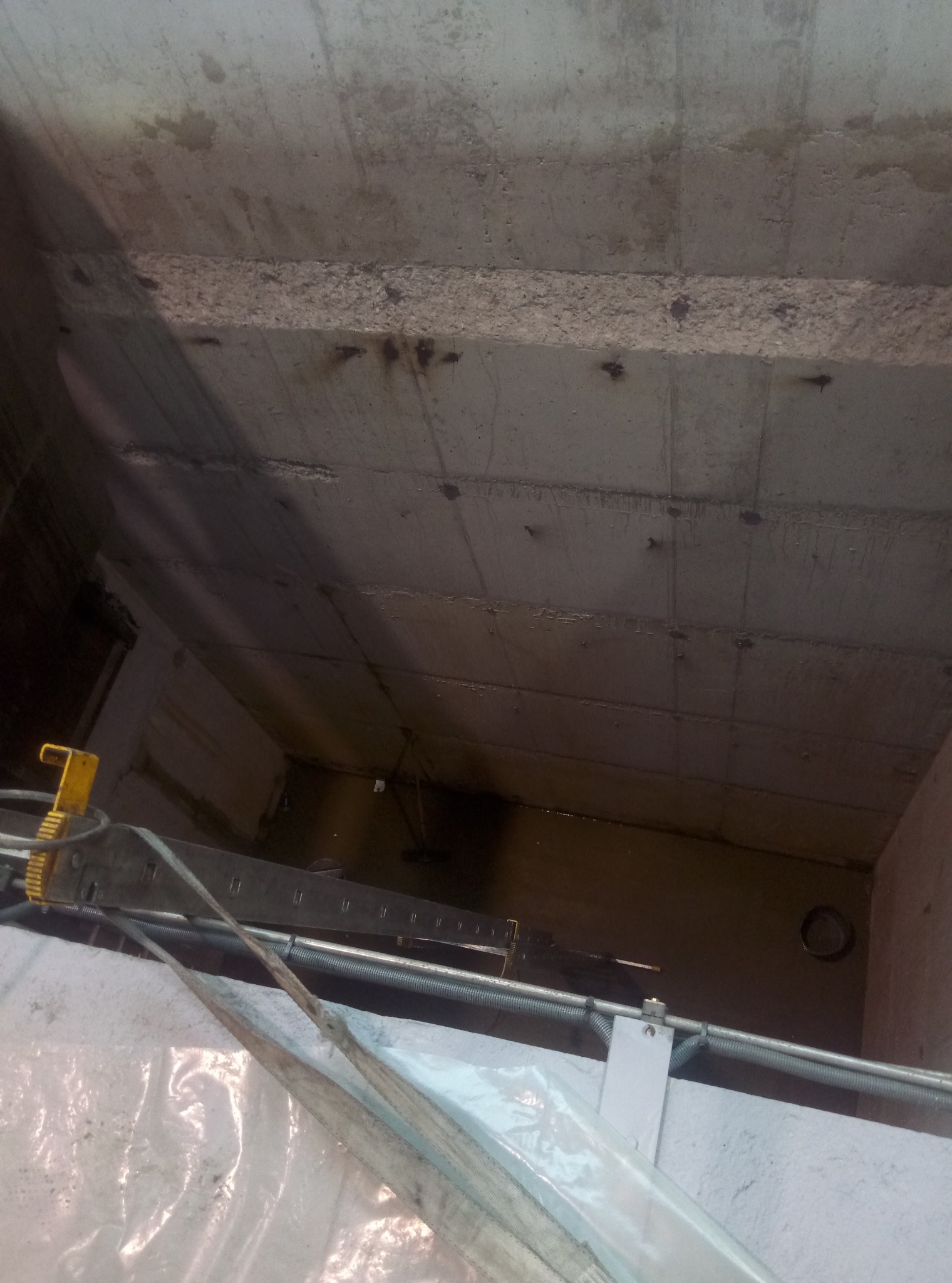 Wnętrze szalunku z betonu, widoczne elementy konstrukcyjne i fragment drabiny, oświetlenie górne.