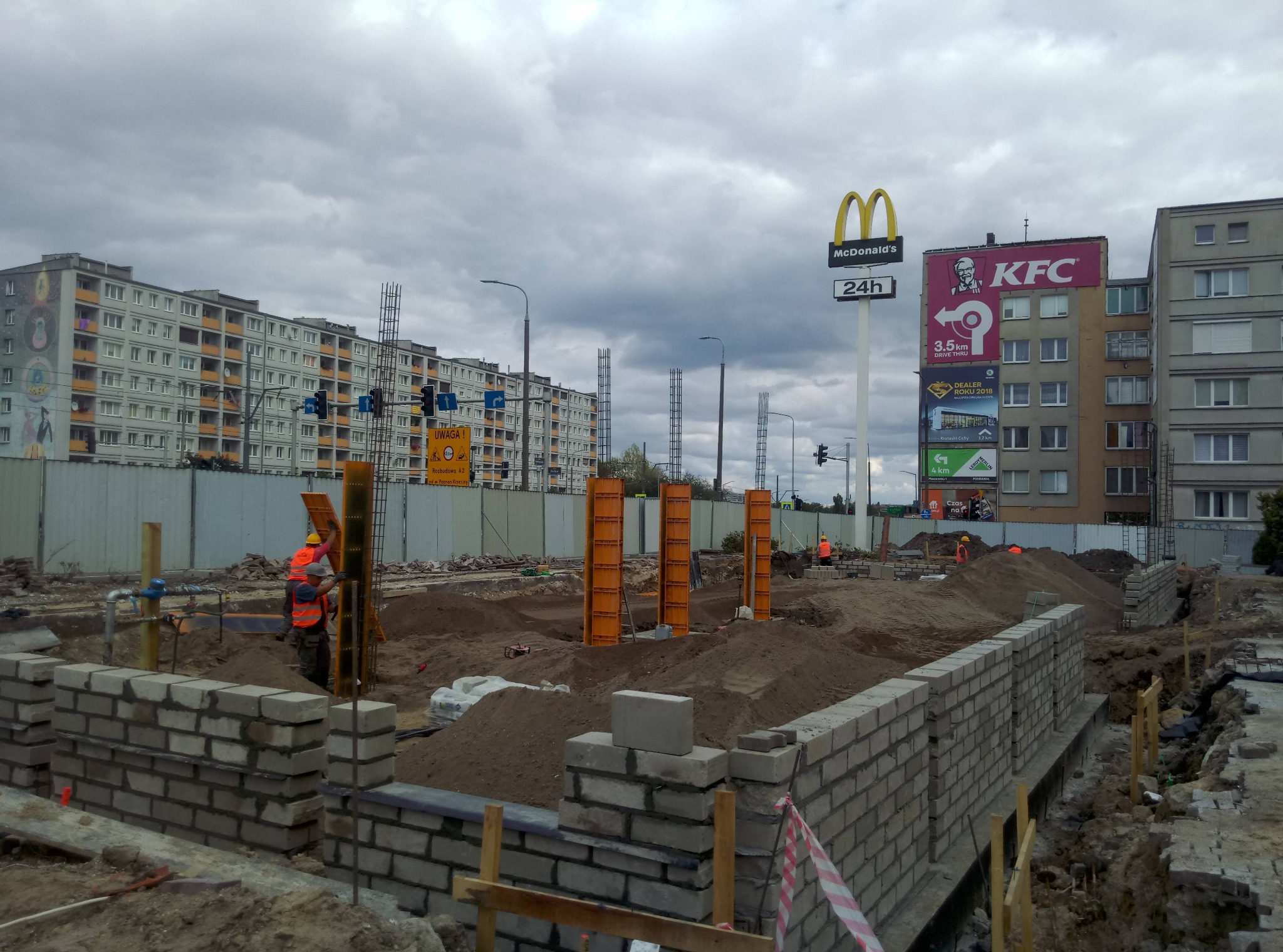 Budowa fundamentów pod budynek w Jarocinie, widoczne szalunki i częściowo wymurowane ściany fundamentowe, w tle zabudowa miejska i reklamy McDonald's i KFC.