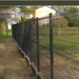 Metalowe ogrodzenie panelowe z podmurówką prefabrykowaną na tle zielonego trawnika i domu jednorodzinnego. Widoczna nazwa firmy OGROBET.