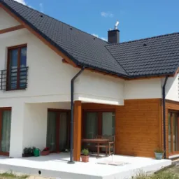 Dwukondygnacyjny dom z jasną elewacją i drewnianą okładziną, ciemnym dachem i balkonami z metalowymi balustradami. W tle komin i błękitne niebo.