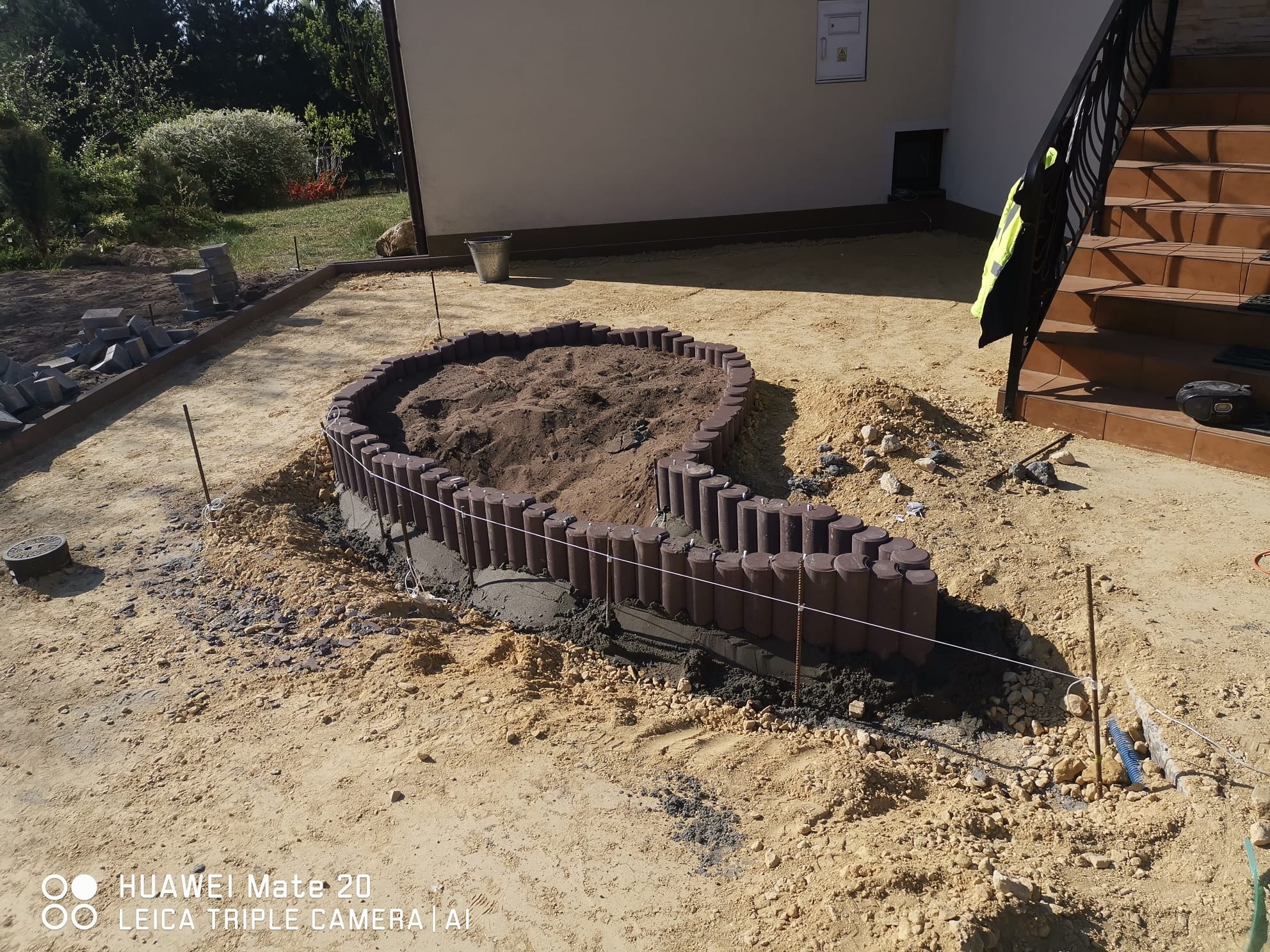 Przygotowanie podłoża pod rabatę kwiatową w Trzebini z wykorzystaniem obrzeży imitujących drewno, wypełnionej ziemią, widoczne narzędzia i materiały budowlane.