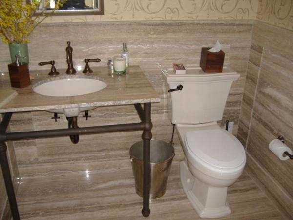 Wykończona łazienka z toaletą i umywalką na metalowym stelażu, wyłożona płytkami imitującymi trawertyn, z dekoracyjną tapetą w tle.