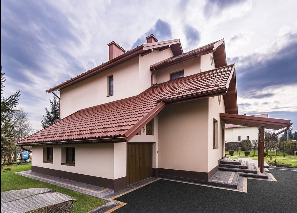 Dom z nowym dachem z dachówki ceramicznej w Koninie. Widoczny fragment ogrodu, błękitne niebo z chmurami i fragment wiaty garażowej.