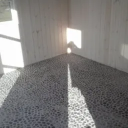 Wnętrze z dekoracyjną podłogą wyłożoną drobnymi kamieniami, jasne panele ścienne i okno z widokiem na zieleń. Promienie słońca tworzą wzory na podłodze.