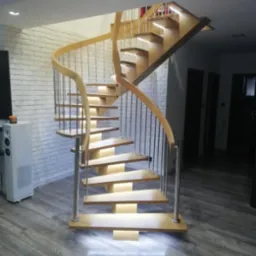 Kręte schody z jasnego drewna i metalowymi balustradami, podświetlone od spodu, na tle białej ściany z cegły i szarej podłogi.