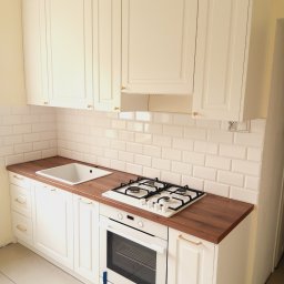 Gasiński Piotr - Jasna kuchnia z drewnianym blatem i białymi szafkami. Widoczna kuchenka gazowa i piekarnik. Styl klasyczny, płytki w stylu metro.