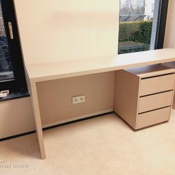 Gasiński Piotr - Beżowe biurko na wymiar z trzema szufladami, ustawione przy oknie. Na parapecie widoczne narzędzia. Minimalistyczny design, jasne wnętrze.