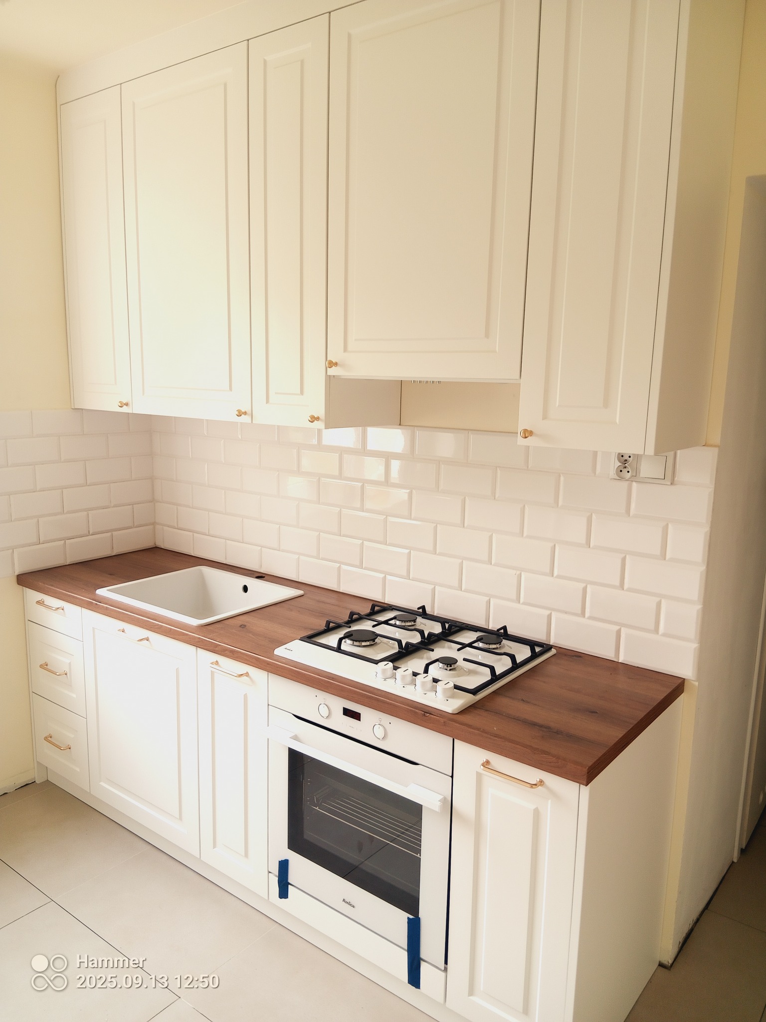 Jasna kuchnia z drewnianym blatem i białymi szafkami. Widoczna kuchenka gazowa i piekarnik. Styl klasyczny, płytki w stylu metro.