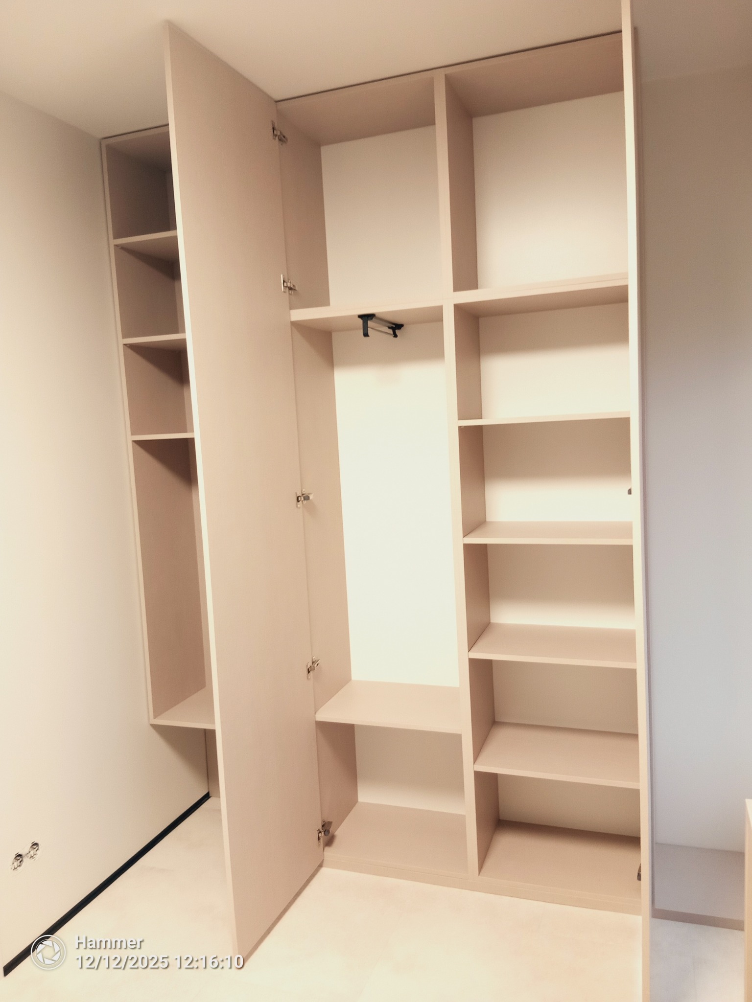 Jasna, otwarta szafa wnękowa z półkami i drążkiem na ubrania, widoczna z perspektywy wnętrza, z otwartymi drzwiami po lewej stronie.