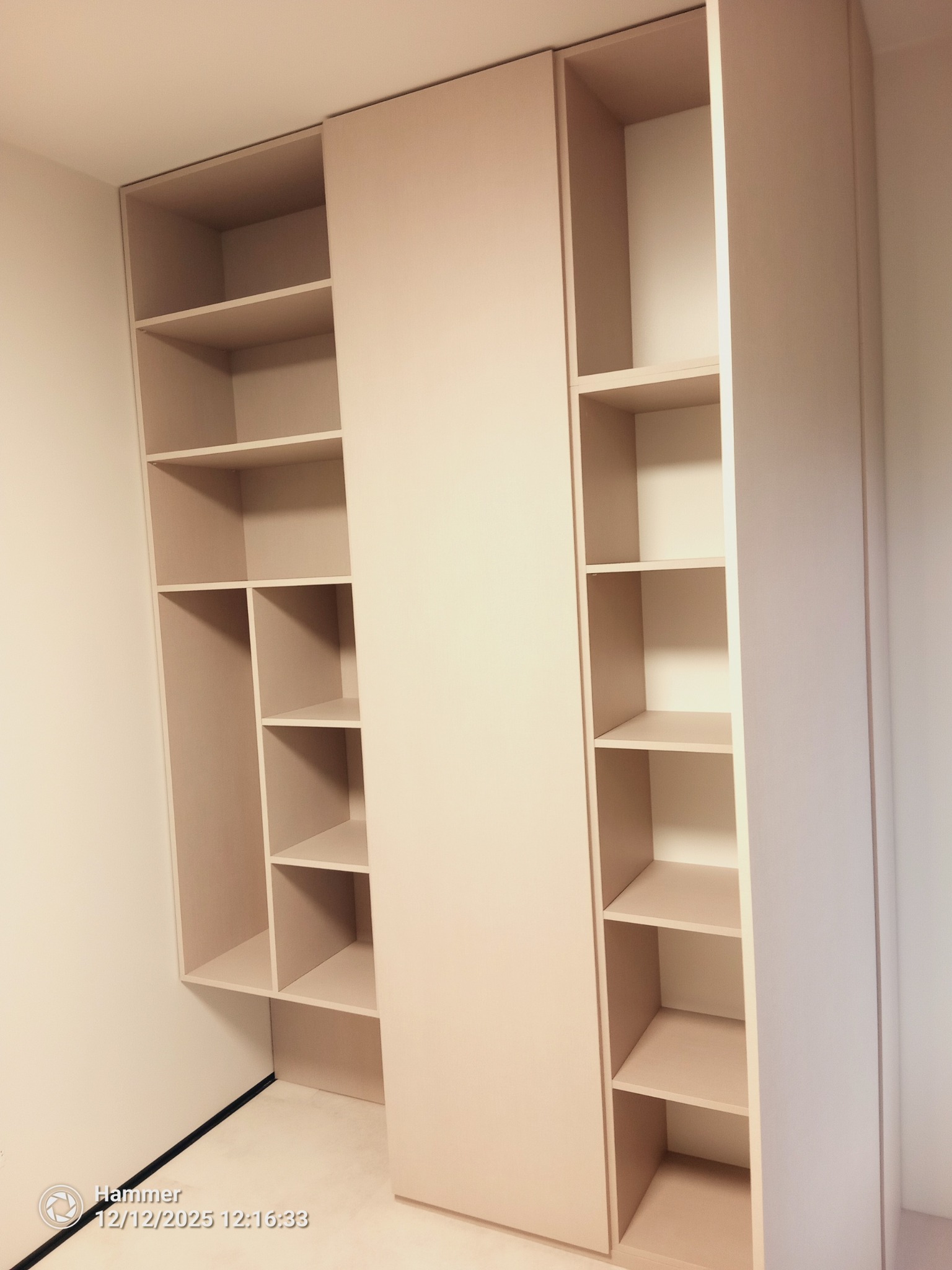 Jasna, minimalistyczna szafa wnękowa z otwartymi półkami, z przesuwnymi drzwiami, wbudowana w narożnik pomieszczenia. Proste linie, brak dekoracji.