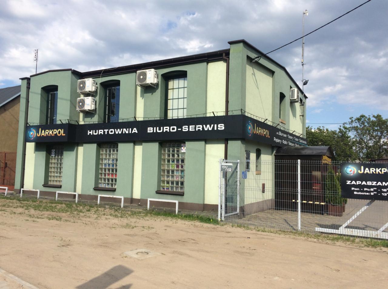 Budynek firmy Jarkpol w Tomaszowie Mazowieckim z szyldem 'Hurtownia Biuro-Serwis', widoczne klimatyzatory na elewacji.