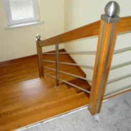 Drewniane schody z metalowymi poręczami i drewnianą balustradą, widok z góry, jasne wnętrze z oknem.