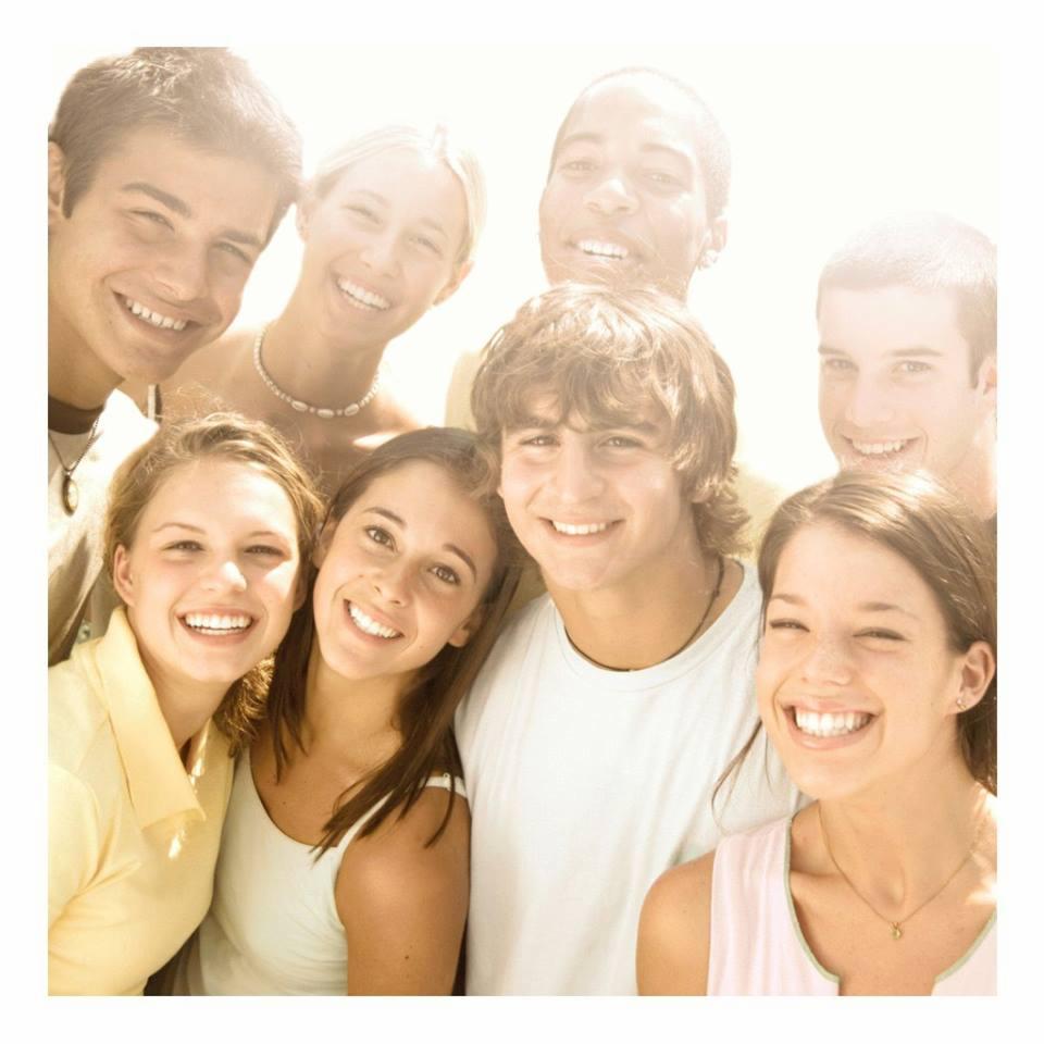 Grupa uśmiechniętych młodych ludzi, w różnym wieku i o różnej karnacji, pozujących do zdjęcia w jasnym oświetleniu, z widocznymi zębami i radosnym wyrazem twarzy.