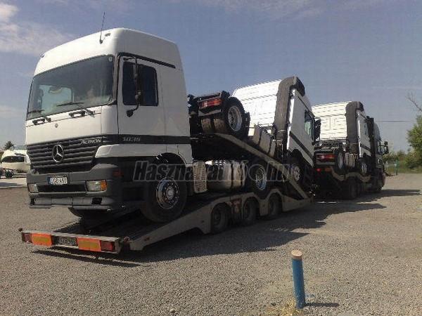 Laweta transportuje trzy białe ciężarówki Mercedes Actros 1845, widoczne tablice rejestracyjne, transport niskopodwoziowy.