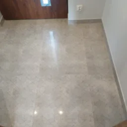 Wykończona podłoga z jasnych, kwadratowych płytek z geometrycznym wzorem 3D, drewniany sufit z wbudowanym oświetleniem LED, szara ściana z gniazdkiem elektrycznym.