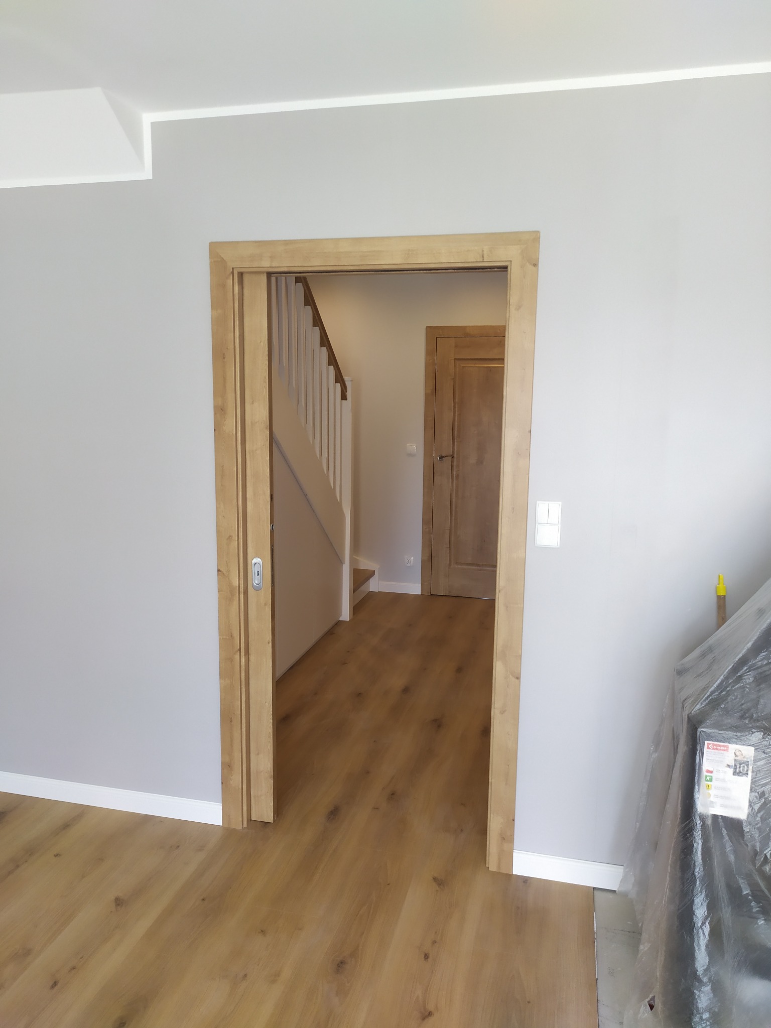 Wnętrze po remoncie: drewniana podłoga, szare ściany, drewniane futryny i drzwi przesuwne, widoczne schody z białymi balustradami w głębi.