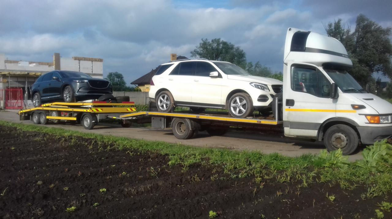 Biała ciężarówka z naczepą transportuje dwa samochody: czarny SUV na żółtej przyczepie i biały SUV na platformie ciężarówki.