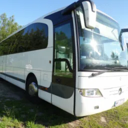 Biały autokar marki Mercedes-Benz z otwartymi drzwiami, zaparkowany na trawie w słoneczny dzień, z widocznym numerem rejestracyjnym WWY 27729.