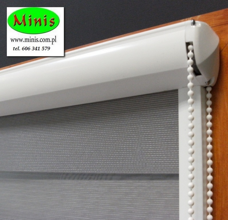 Szara przesłona okienna typu dzień i noc z białym mechanizmem i łańcuszkiem, widoczne logo producenta w lewym górnym rogu.