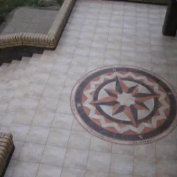 Beżowa podłoga z płytek z dekoracyjnym wzorem kompasu. Schody z ceglaną barierką. Widok z góry.