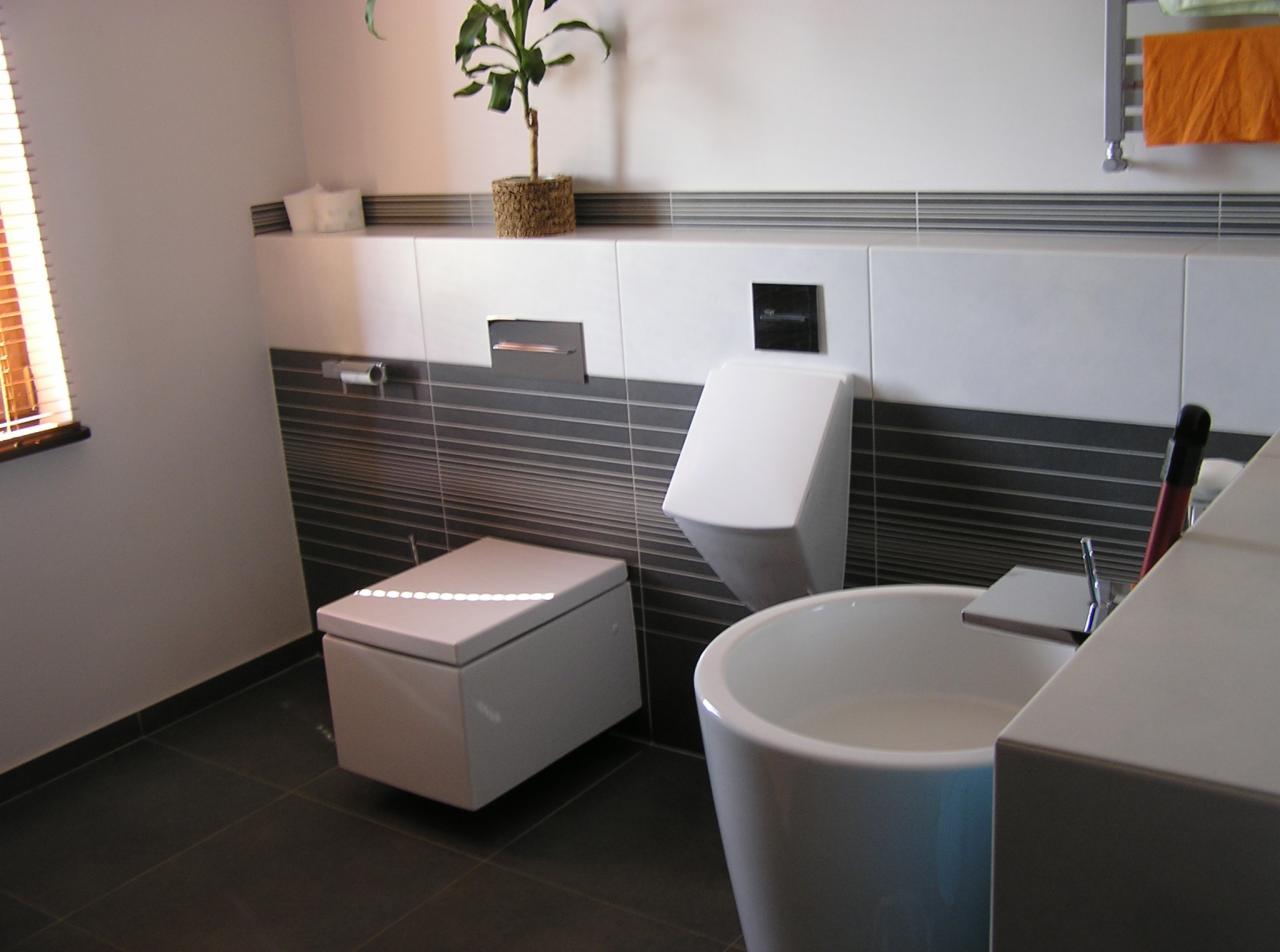 Nowoczesna łazienka z podwieszaną toaletą i umywalką w kształcie misy. Szare płytki z poziomymi paskami, białe ściany, roślina w doniczce, minimalistyczny design.