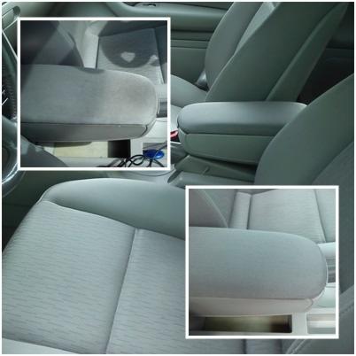 Szczegółowe ujęcie jasnoszarej tapicerki samochodowej, z naciskiem na czysty podłokietnik i fragment fotela. Widoczne detale faktury materiału i subtelne przeszycia.