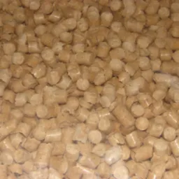 Jasne, cylindryczne granulki pelletu z widocznymi włóknami drzewnymi, ułożone gęsto, z lekkim efektem przezroczystości w dolnej części kadru.