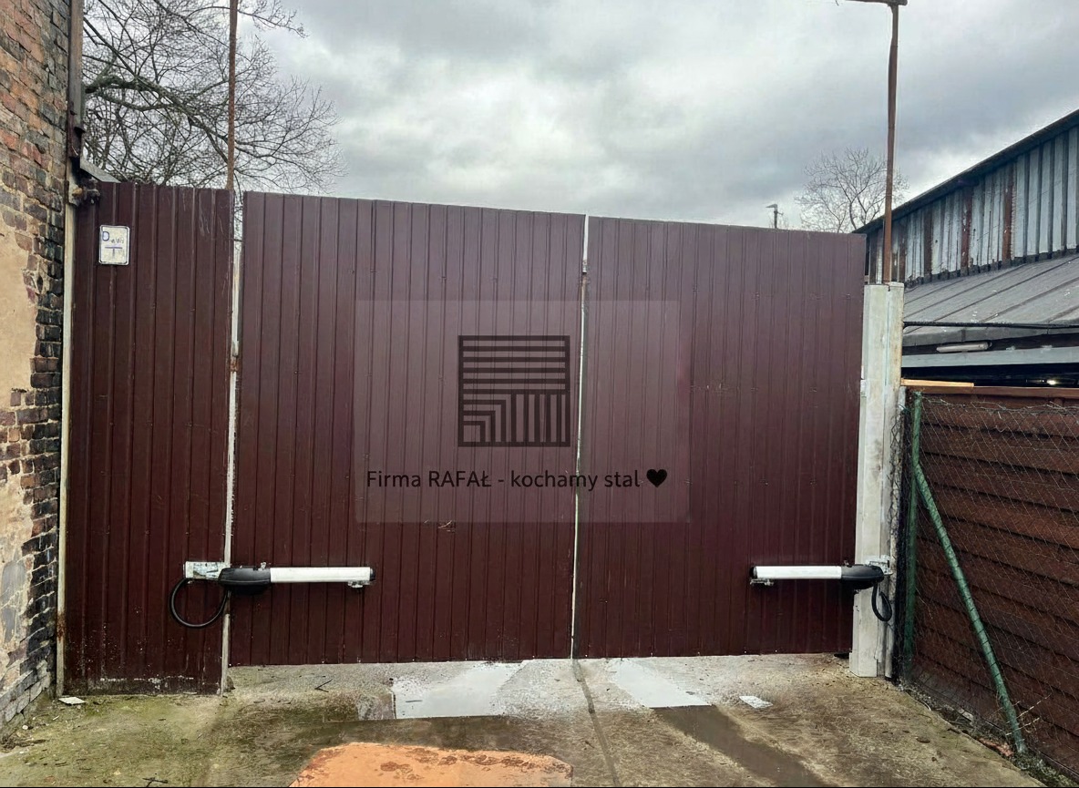 Brązowa brama wjazdowa dwuskrzydłowa z automatyką, widoczne siłowniki. Brama z blachy trapezowej, na posesji prywatnej. Ujęcie z poziomu gruntu, pochmurne niebo.