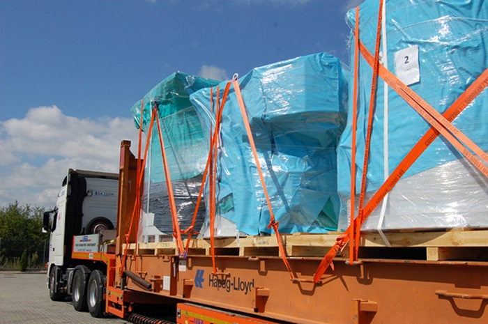 Załadunek na naczepie ciężarówki: zabezpieczone pomarańczowymi pasami transportowymi, owinięte folią stretch i niebieską plandeką palety z towarem, oznaczone numerem '2'.