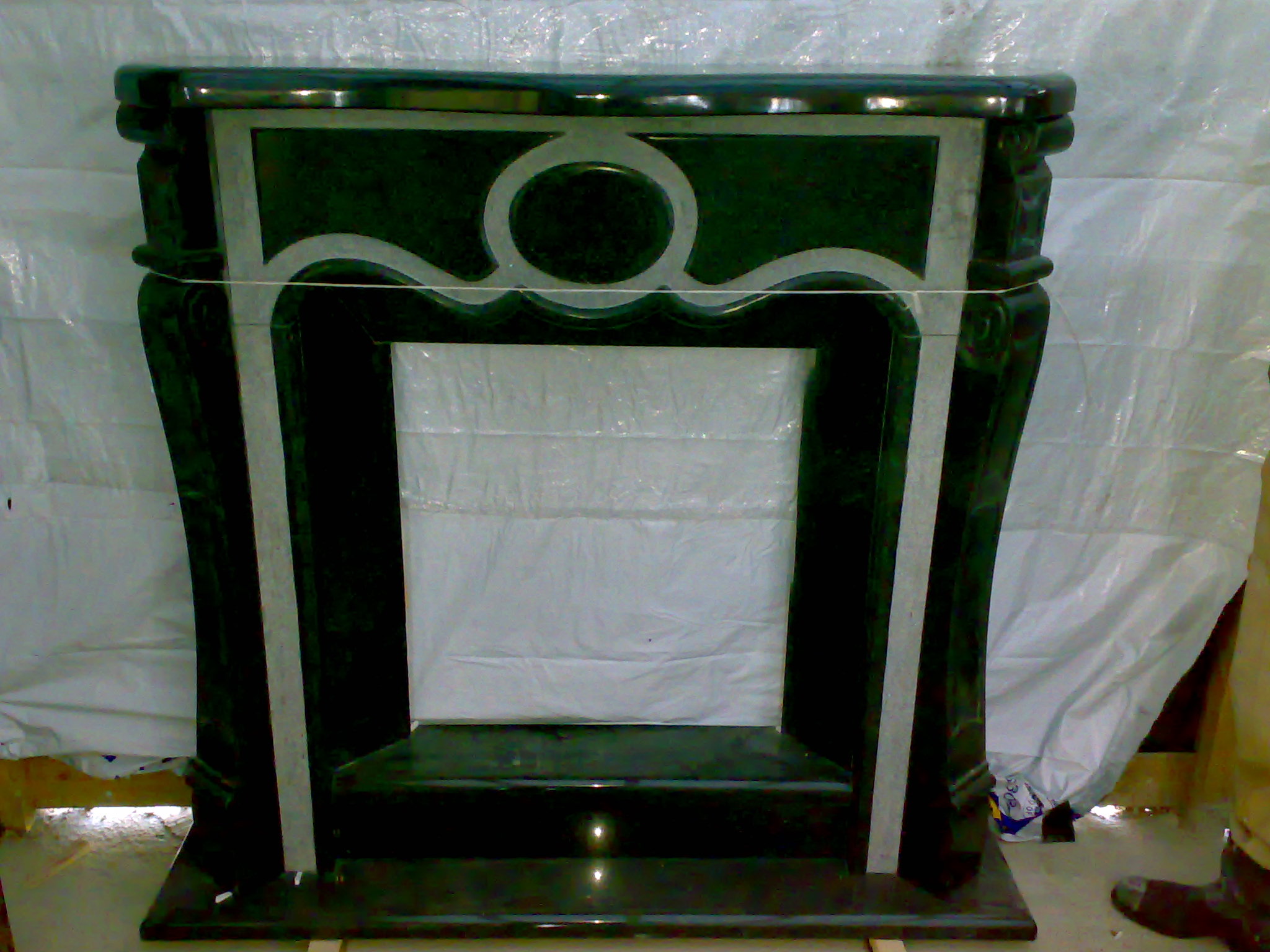 Marmurowy obudowa kominka w odcieniach zieleni i bieli, z dekoracyjnymi elementami, na tle folii ochronnej.