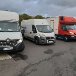 Trzy busy transportowe r&oacute;żnych marek (Renault Master, Fiat Ducato, Iveco) zaparkowane obok siebie na parkingu, z widocznymi numerami rejestracyjnymi i oznaczeniami firm transportowych.