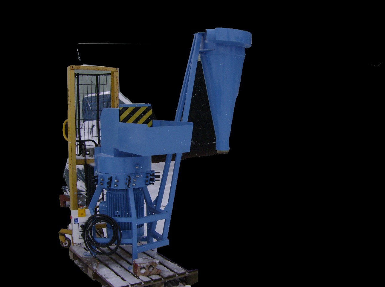 Niebieska kruszarka na palecie w zimowej scenerii, widoczny podajnik, silnik elektryczny i fragment wózka widłowego.
