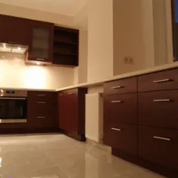 Nowoczesna kuchnia z ciemnymi drewnianymi szafkami, srebrnymi uchwytami, białym blatem i błyszczącą podłogą z płytek; widoczny piekarnik Samsung i biały grzejnik.