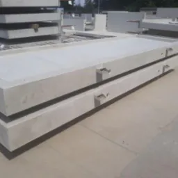 Stos prefabrykowanych płyt betonowych z uchwytami transportowymi, ułożonych na placu budowy, widoczne z bliska.