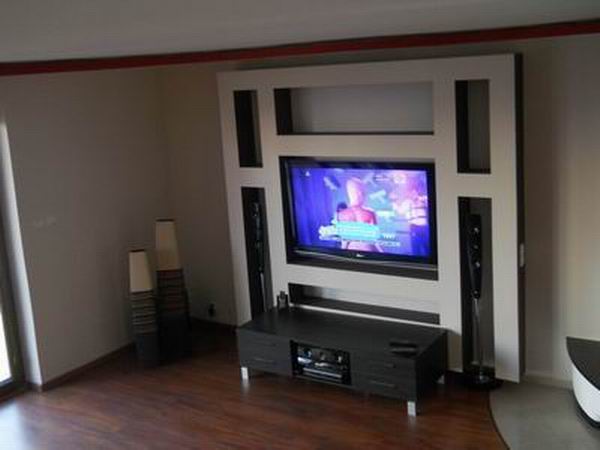 Telewizor wbudowany w ścianę z szafką RTV i głośnikami, aranżacja wnętrza z drewnianą podłogą i dekoracyjnymi wazonami.