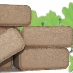 Ułożone w stos prostokątne brykiety z widoczną strukturą drewna na białym tle z zielonymi liśćmi dębu.