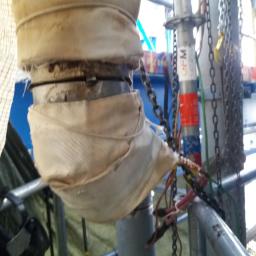 PROLMAR - Rura owinięta materiałem izolacyjnym na rusztowaniu, widoczne łańcuchy i przewody.