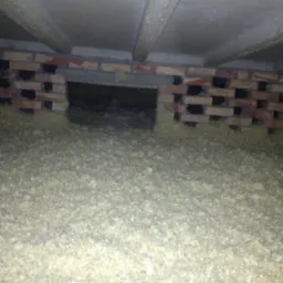 Nisko położone ujęcie przestrzeni pod podłogą z ceglaną ścianą fundamentową z otworami wentylacyjnymi i luźnym materiałem izolacyjnym na ziemi.