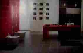 Nowoczesna łazienka z czerwonymi akcentami: ściana z czerwonymi płytkami, czerwony blat z umywalką, ciemna podłoga i białe sanitariaty. Na ścianie za toaletą galeria czarno-białych zdjęć w ramkach.