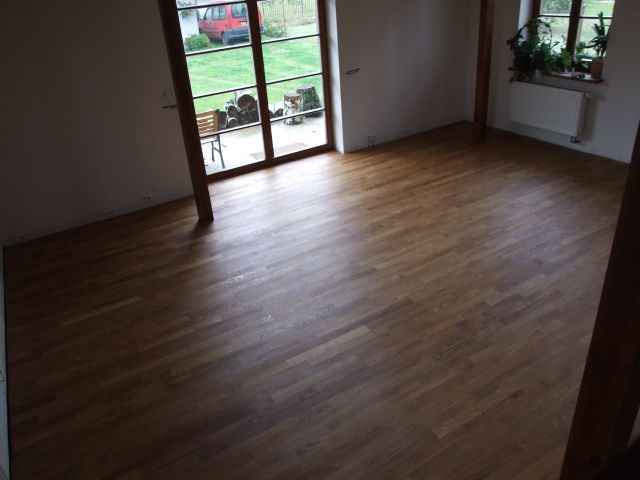 Wycyklinowana, lakierowana podłoga parkietowa z wyraźnym usłojeniem, widok na taras przez przeszklone drzwi balkonowe, naturalne światło.