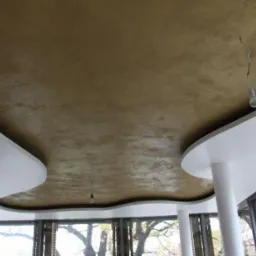 Złota, teksturowana powierzchnia sufitu z dekoracyjnymi, białymi elementami wykończeniowymi i wiszącą żarówką na kablu, widok z dołu.